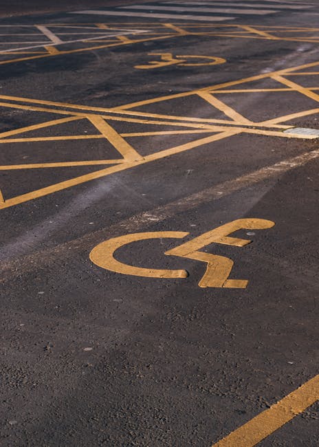 A blue parking sign with a white wheelchair symbol and a capital letter 'P' is mounted on a metal post against a dark grey exterior wall. The sign indicates accessible parking, likely designated for individuals with disabilities. The wall's surface appears smooth and uniform, and there are no other objects or vehicles visible in the image. The sign is positioned in front of the wall, suggesting it is mounted on a paved area such as a driveway or parking space typically used during home relocations. This setting can be associated with moving services provided by Man With a Van Sydenham, especially in contexts requiring parking permits or suspensions for efficient furniture transport, packing, or loading operations during a home move. The lighting is neutral, with subtle shadows cast by the sign, indicating it might be during daylight hours.