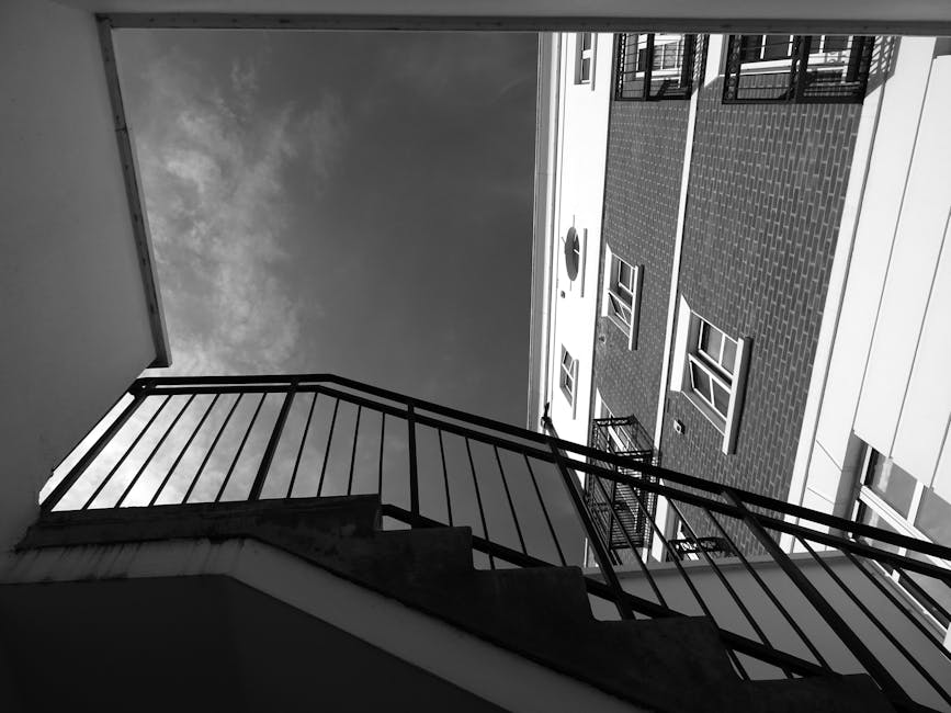 A staircase inside a residential property with a marble-tiled landing and wooden stairs leading up to an open doorway. The staircase features a dark wooden handrail and white balustrades, with natural light coming through a window at the top. On the left side, a silver step ladder leans against the wall, and several potted plants are positioned on the window sill, adding greenery to the space. The wall beside the stairs is painted in a neutral light colour, and a spherical ceiling light fixture is visible on the right. This scene depicts interior elements of a home in the context of a house move, with potential focus on the challenges of transporting furniture and belongings through the staircase during a relocation managed by Man With a Van Sydenham.
